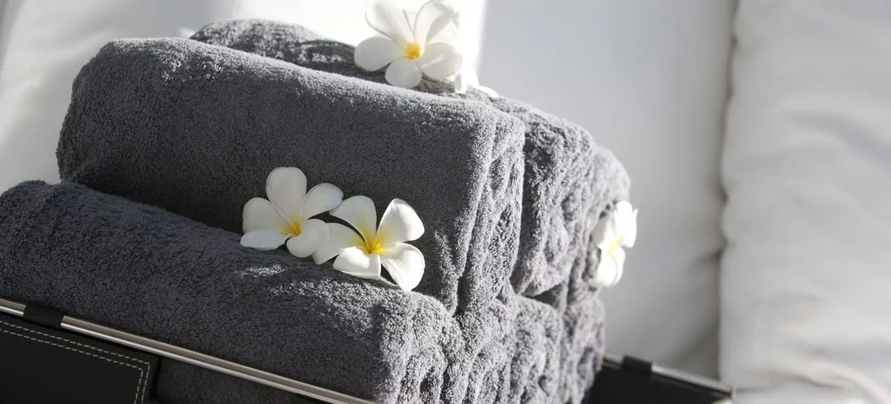 Freshly rolled grey towels adorned with delicate white frangipani flowers at The Lombok Lodge, a luxury resort in Lombok