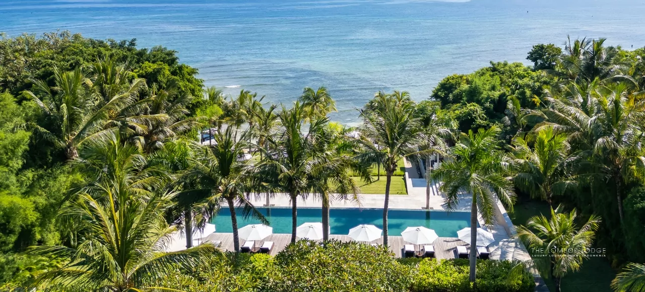 A breathtaking aerial view of The Lombok Lodge, a luxury beachfront resort in Lombok, featuring an infinity pool, lush tropical gardens, and a serene ocean backdrop