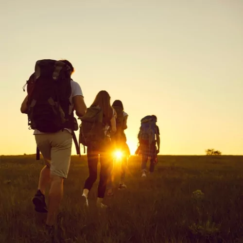 A group of trekkers hiking towards the sunset, carrying backpacks, symbolizing an adventurous Mount Rinjani trekking experience in Lombok, Indonesia