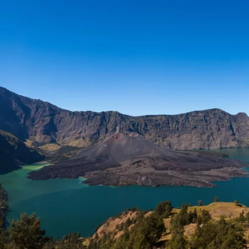 A stunning view of Mount Rinjani’s crater lake, Segara Anak, with a volcanic peak in the center, surrounded by dramatic mountain landscapes in Lombok, Indonesia.