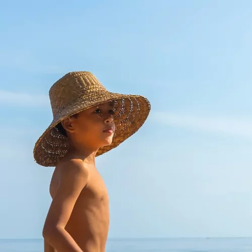 Young child wearing a straw sun hat gazing at the ocean during a family vacation in Lombok