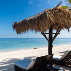 Thatched umbrella with sun loungers on a sandy beach overlooking the ocean at Gili Islands, Bali