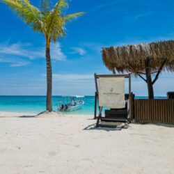 Beach chair under a thatched shade facing turquoise waters and boats at Gili Islands, Lombok