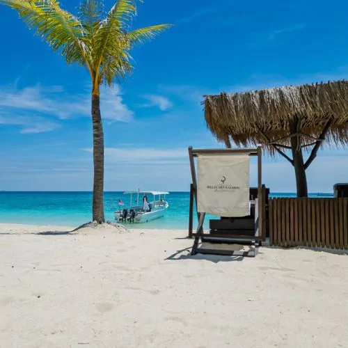 Beach chair under a thatched shade facing turquoise waters and boats at Gili Islands, Lombok