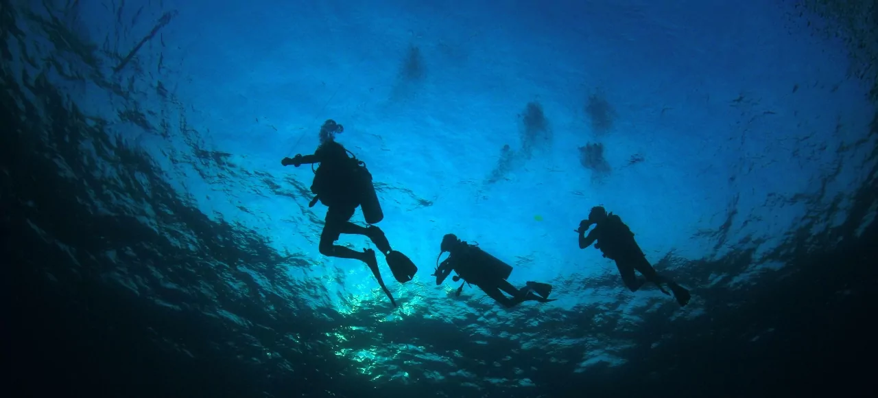 Three scuba divers exploring the clear blue waters of Gili Meno, Lombok